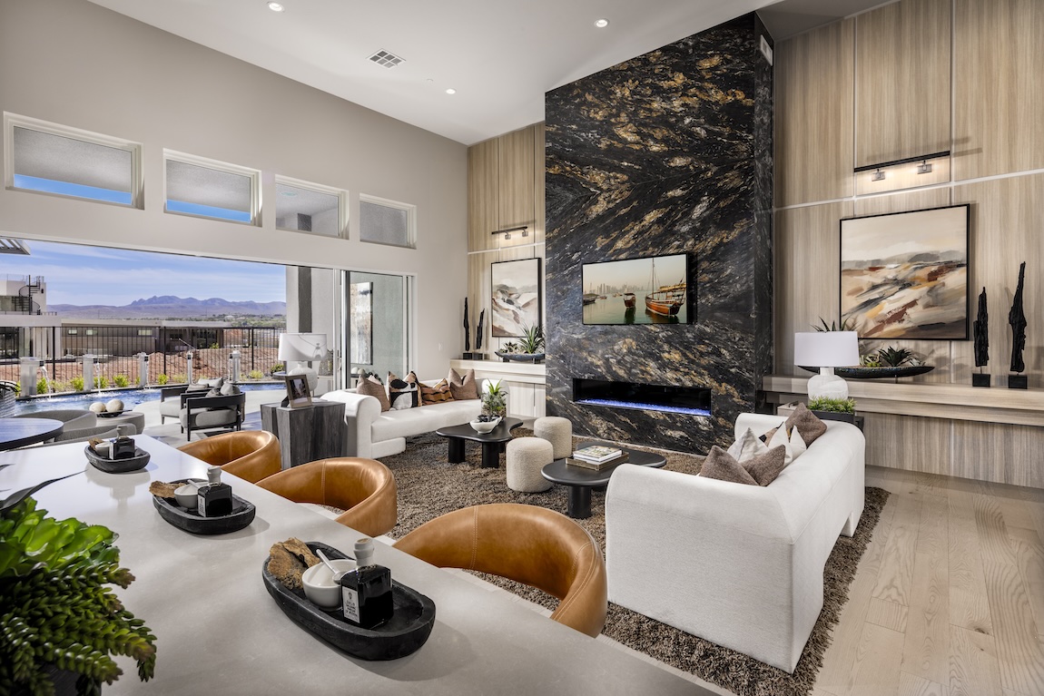 Open great room with a dramatic stone fireplace wall, neutral seating, leather accent chairs, and large windows opening to an outdoor view.