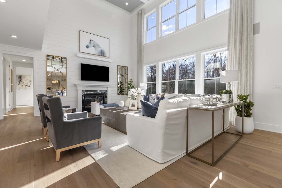 Bright great room with double-height windows, white shiplap fireplace wall, neutral seating, light wood floors, and natural light filling the space.