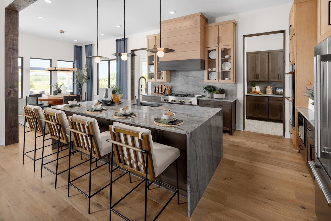 Spacious kitchen with a gray stone waterfall island, wood cabinetry, mixed-metal pendant lights, and bar seating in an open-concept layout.