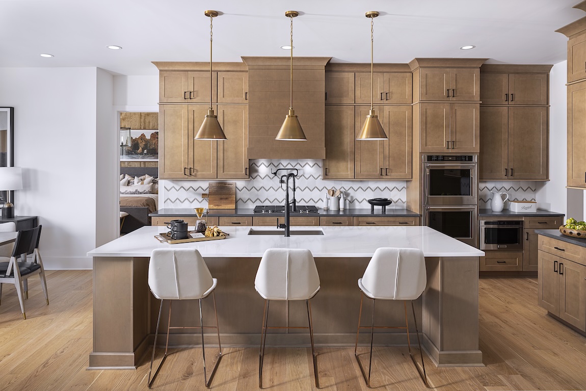 Contemporary kitchen with warm wood cabinetry, a white island with seating, brass pendant lights, patterned backsplash, and built-in appliances.