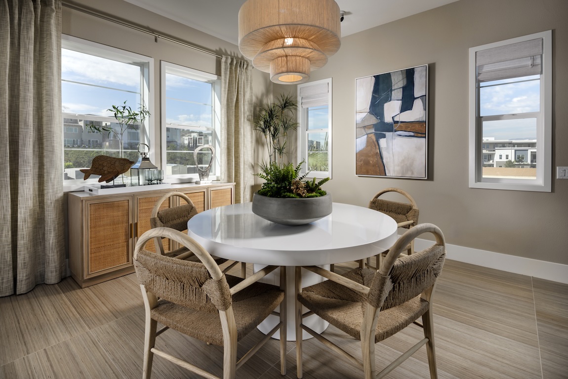 Dining room with woven chairs, round table, and soft neutral walls in Universal Khaki, the Sherwin-Williams Color of the Year 2026, creating a warm, inviting atmosphere.