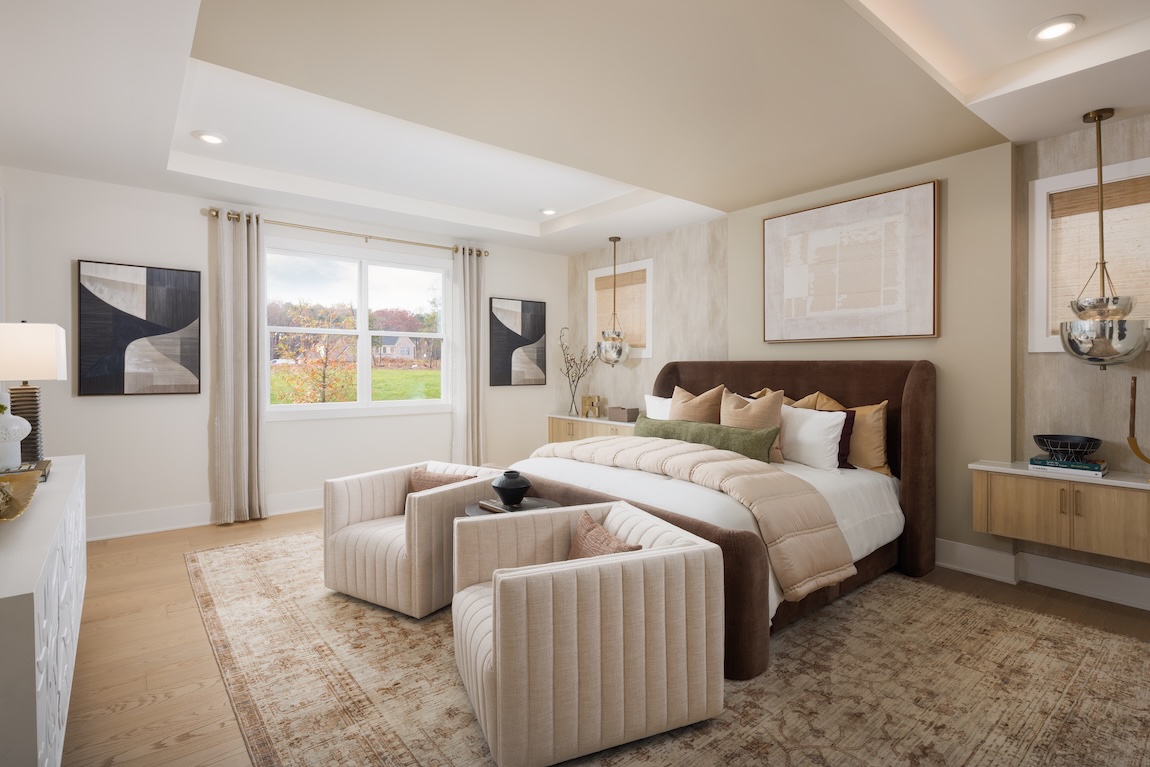 Primary bedroom with upholstered bed, neutral bedding, and walls featuring Universal Khaki, the Sherwin-Williams Color of the Year 2026, creating a cozy, layered retreat.
