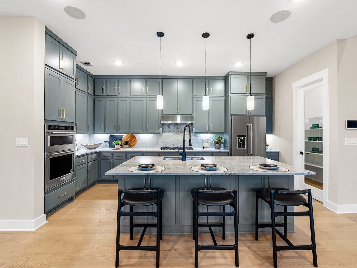 Soft gray-blue kitchen cabinets with marble countertops and warm wood flooring for a balanced neutral cabinet palette.