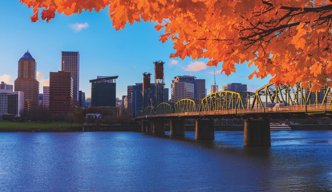 Downtown Portland skyline and bridge over the Willamette River framed by vibrant autumn foliage.