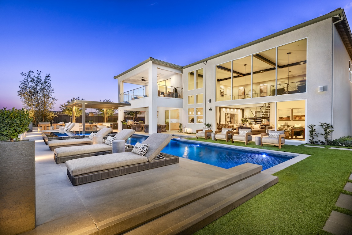 exterior of home with warm interior lighting and pool