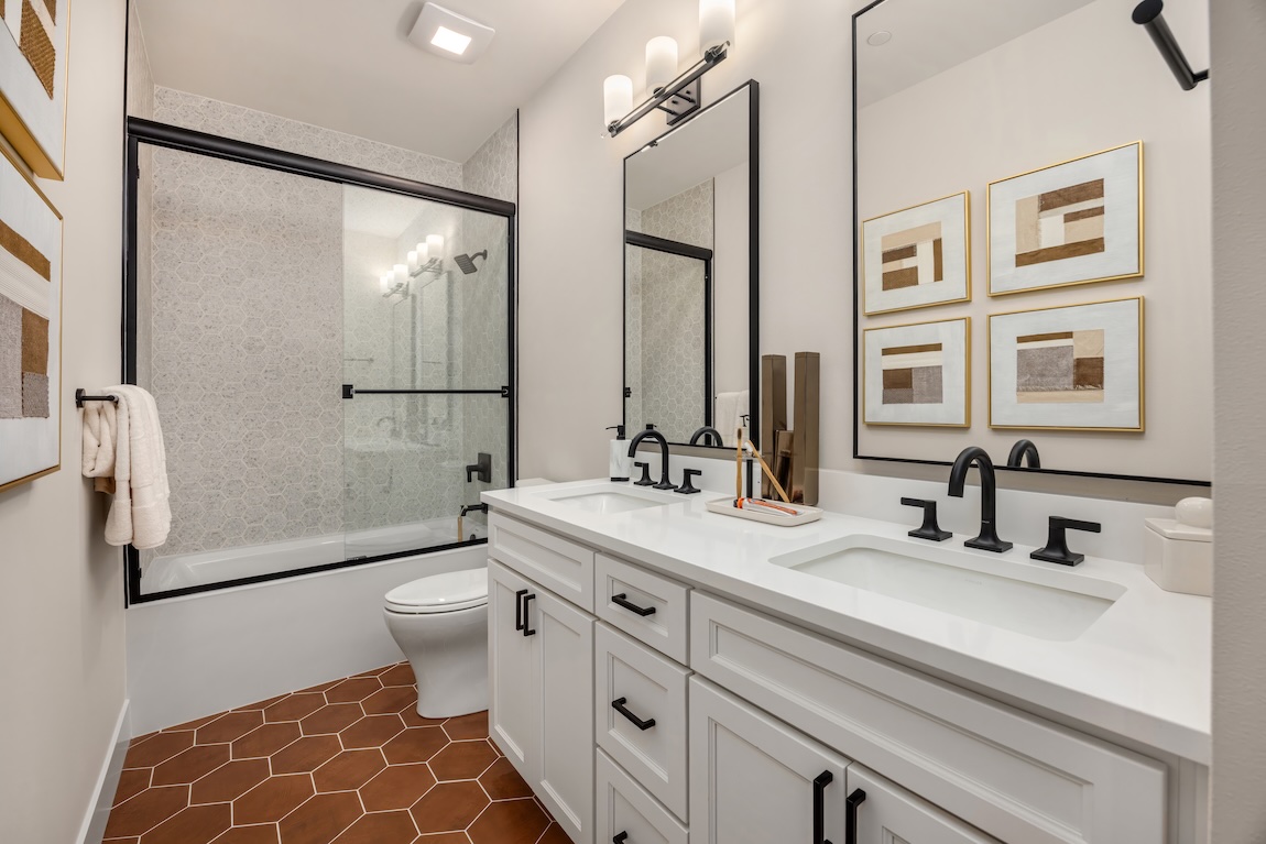 Bathroom with terracotta hexagon floor tile, white double vanity, and black fixtures