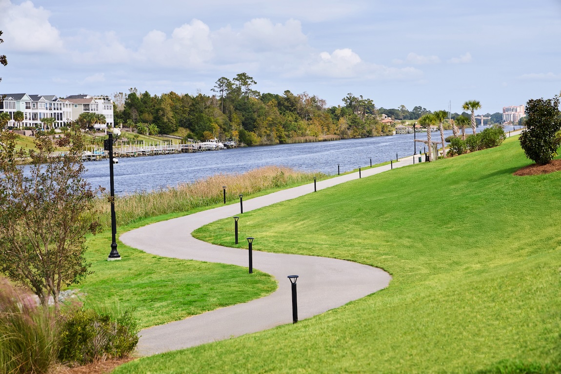 Scenic waterfront walking trail surrounded by green space and residential homes.