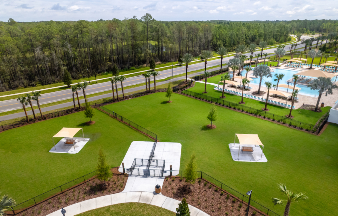 Pet-friendly community dog park with open lawn, shaded seating, and nearby resort-style pool.