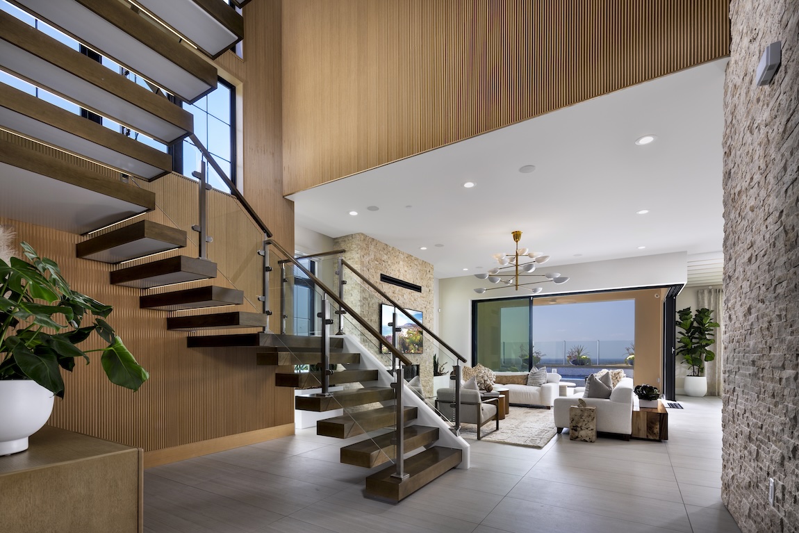 Floating wood treads and a glass-railed staircase rise beside a vertical wood accent wall in an open living room.