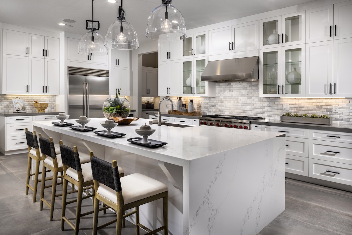 White shaker-style kitchen cabinets with glass-front uppers, a subway tile backsplash, stainless steel appliances, and a large waterfall island.