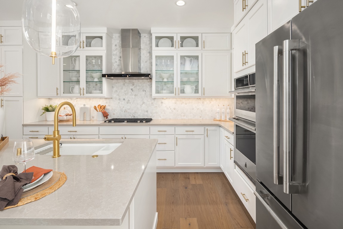 Bright contemporary kitchen featuring white cabinetry with glass display cabinets, brass hardware, and a spacious island with a matching faucet.