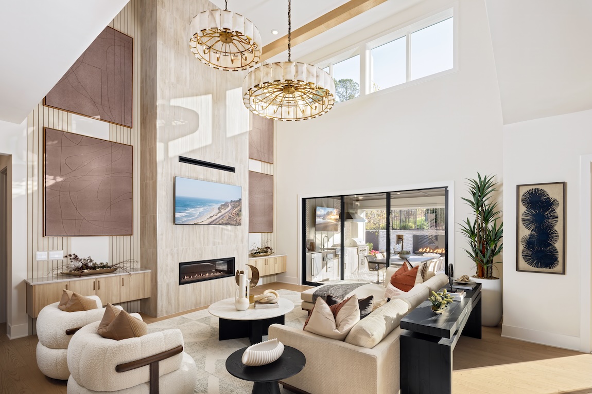 Double-height great room with statement chandeliers, a linear fireplace, architectural wall panels, and neutral furnishings.