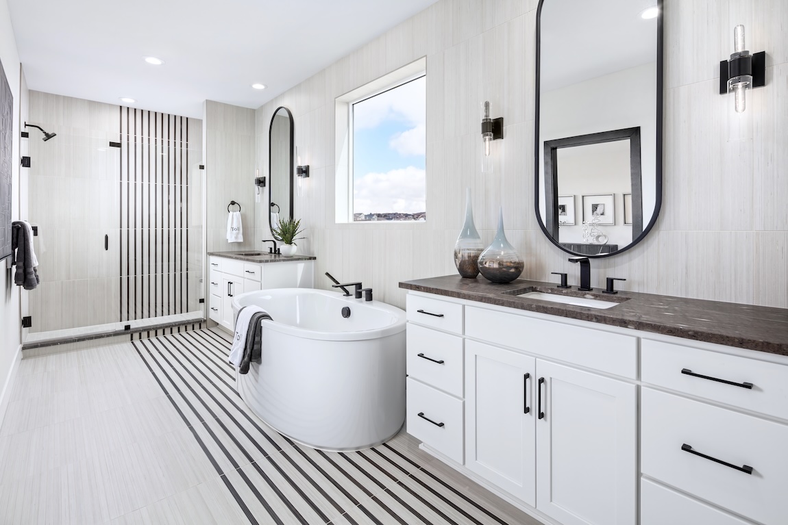 Black-and-white primary bathroom with a freestanding tub, striped tile flooring, dual vanities, and glass-enclosed shower.