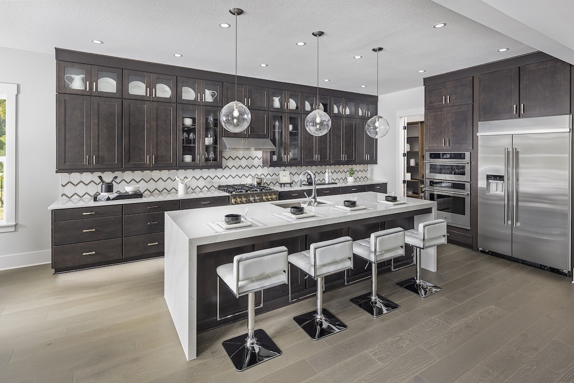 Dark wood kitchen cabinets with glass-front display sections, a geometric tile backsplash, and an oversized white island with pendant lighting.