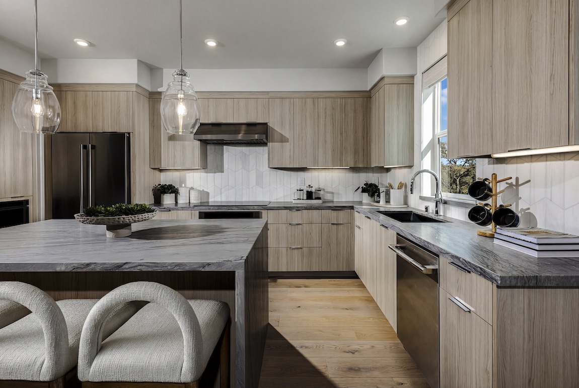 Modern kitchen with streamlined wood cabinetry, stone countertops, sculptural seating, and glass pendant lights.