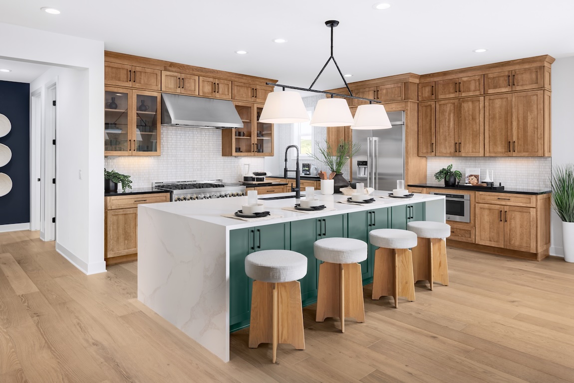Warm natural wood cabinetry with glass display doors complements a teal kitchen island, white countertops, and modern pendant lighting.