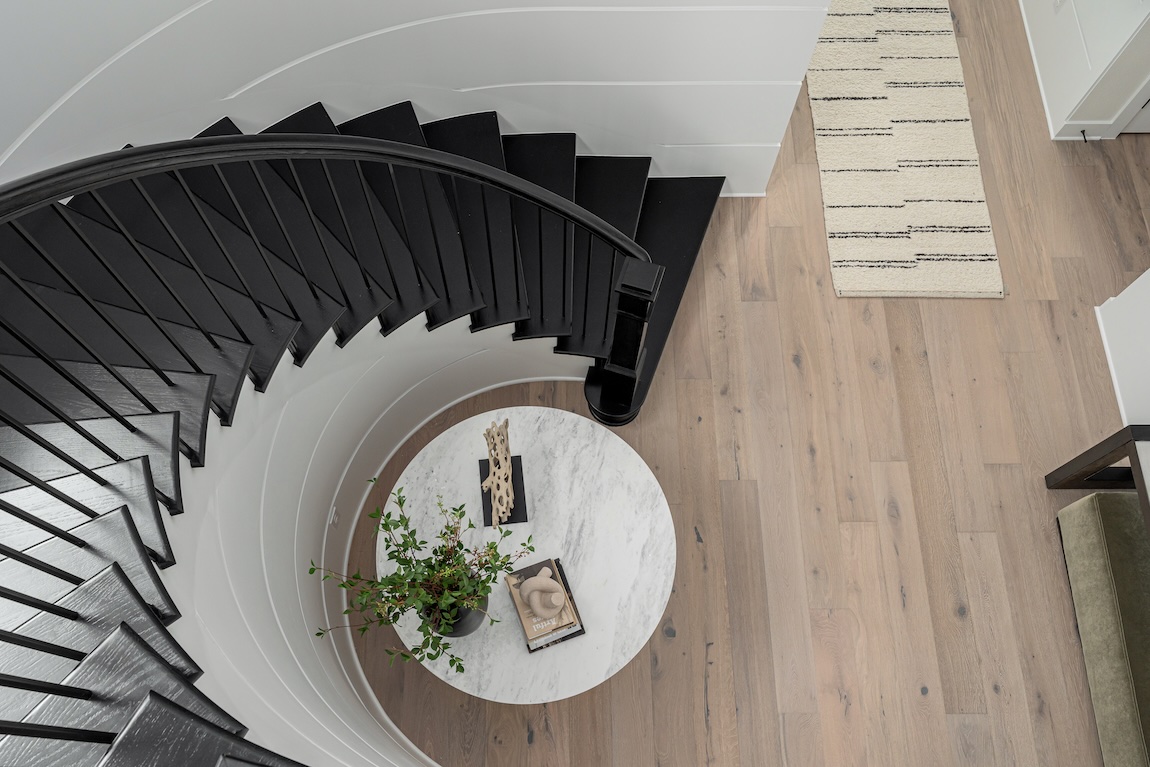 A curved black staircase wraps around a round foyer table, viewed from above.