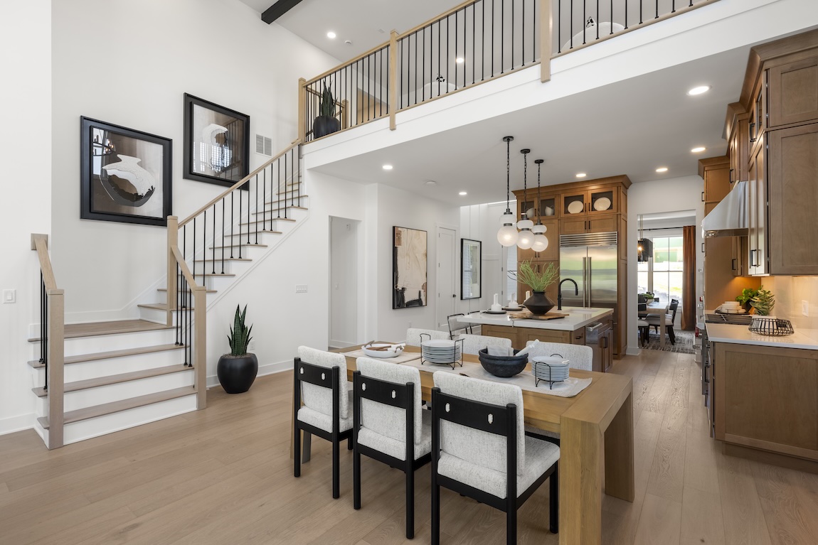 A staircase with pale treads and dark railings connects the dining area to an upper-level gallery in an open-plan home.