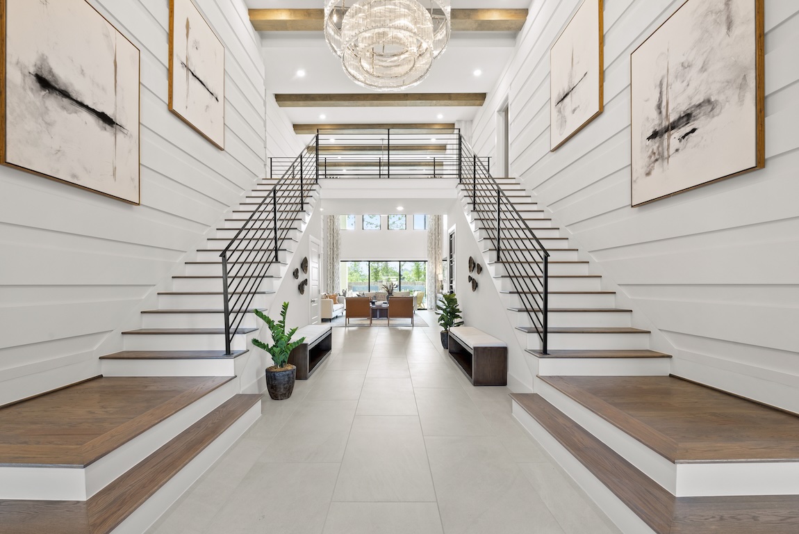 Two staircases with pale wood treads and dark railings frame a bright, symmetrical foyer.