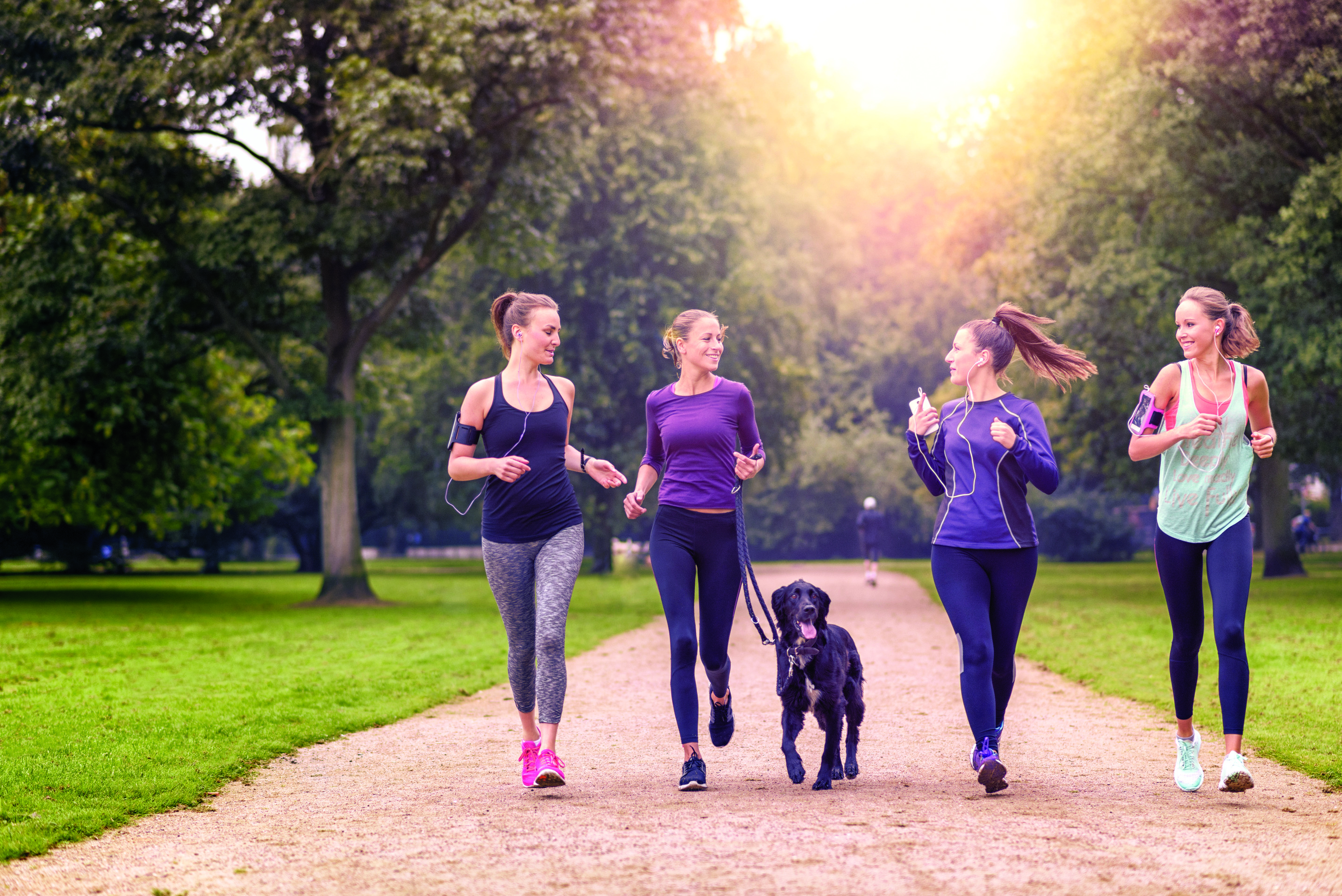 Four friends jogging with a dog in a park.