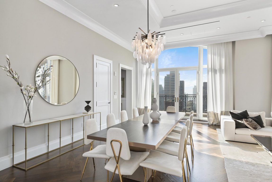 A dining room with a white color scheme and doors that open up to a terrace overlooking the city.