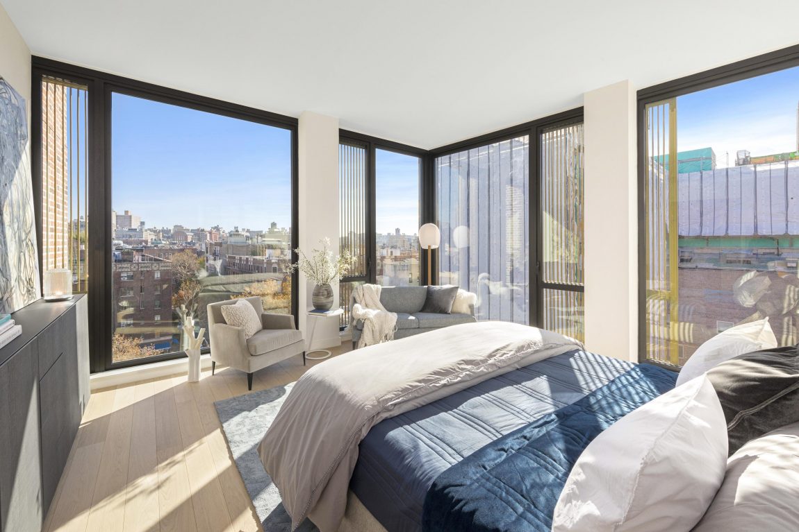 A bedroom with large windows and a view overlooking the city.