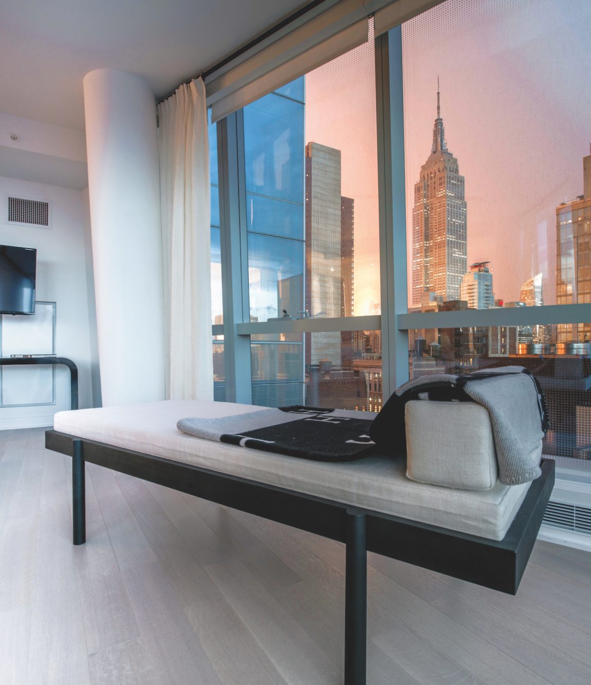 A modern couch next to a window with a view of the Empire Sate Building at sunset.