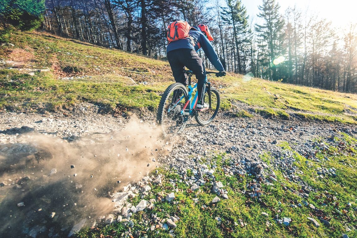 Rear view of male biker riding mountain bike on mountain trail.
