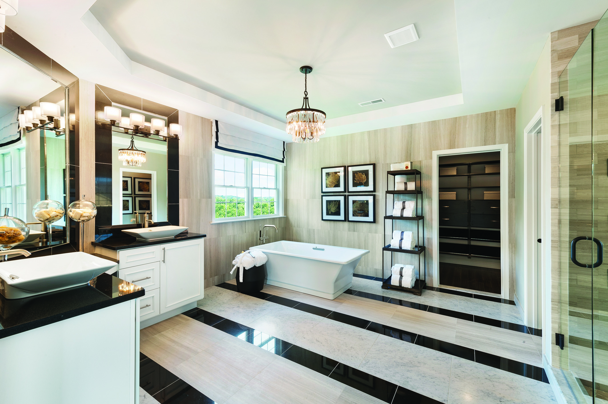 Bathroom with raised ceiling, lavish chandelier, freestanding bathtub, and dual display vanity