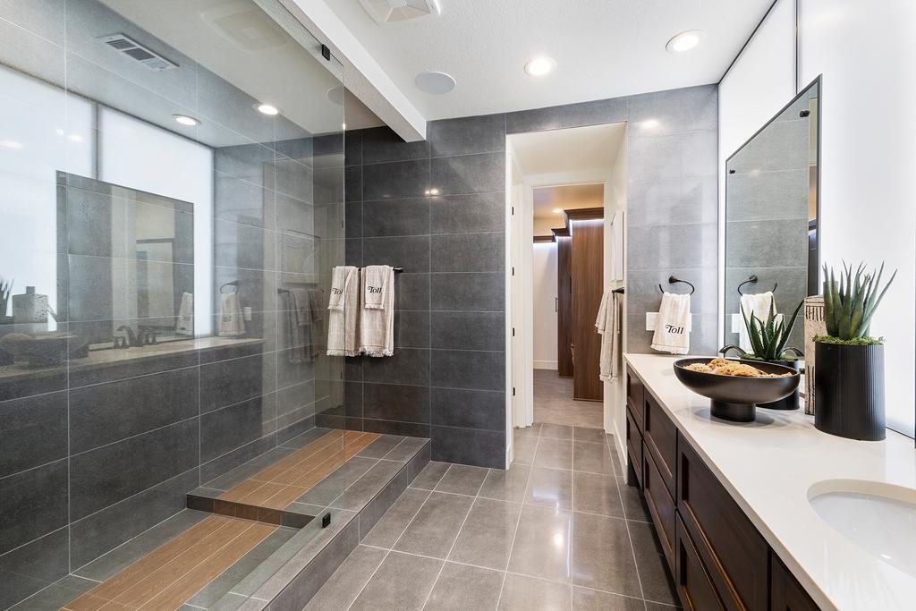 Bathroom with gray floor and wall tiling, walk-in shower, and dual vanity display
