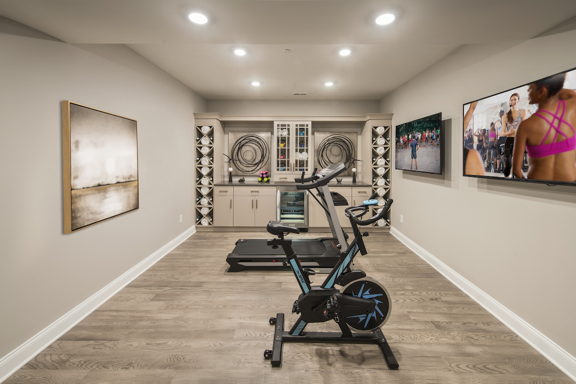 Home gym featuring treadmill and indoor bike with dual TV display