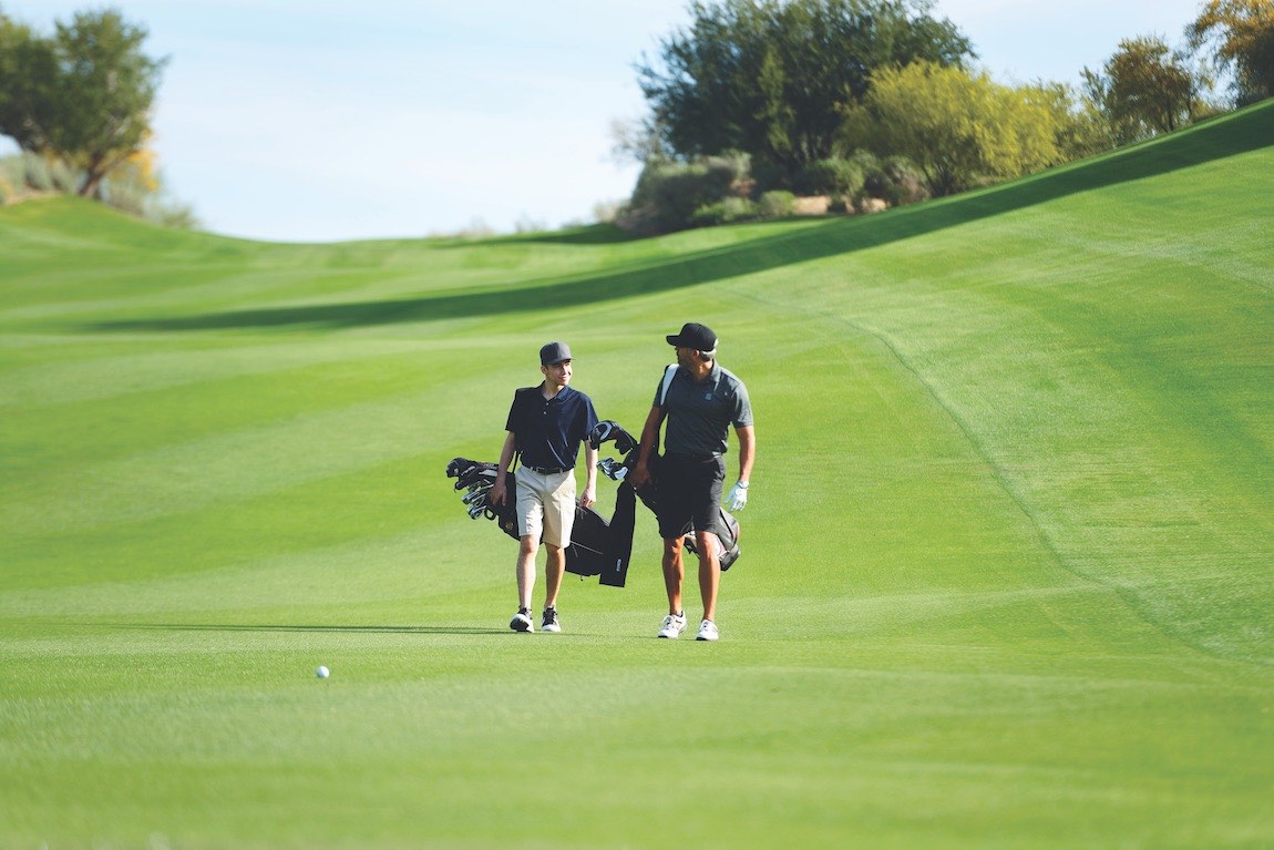 Two men walking on a golf course with golf clubs on a sunny day