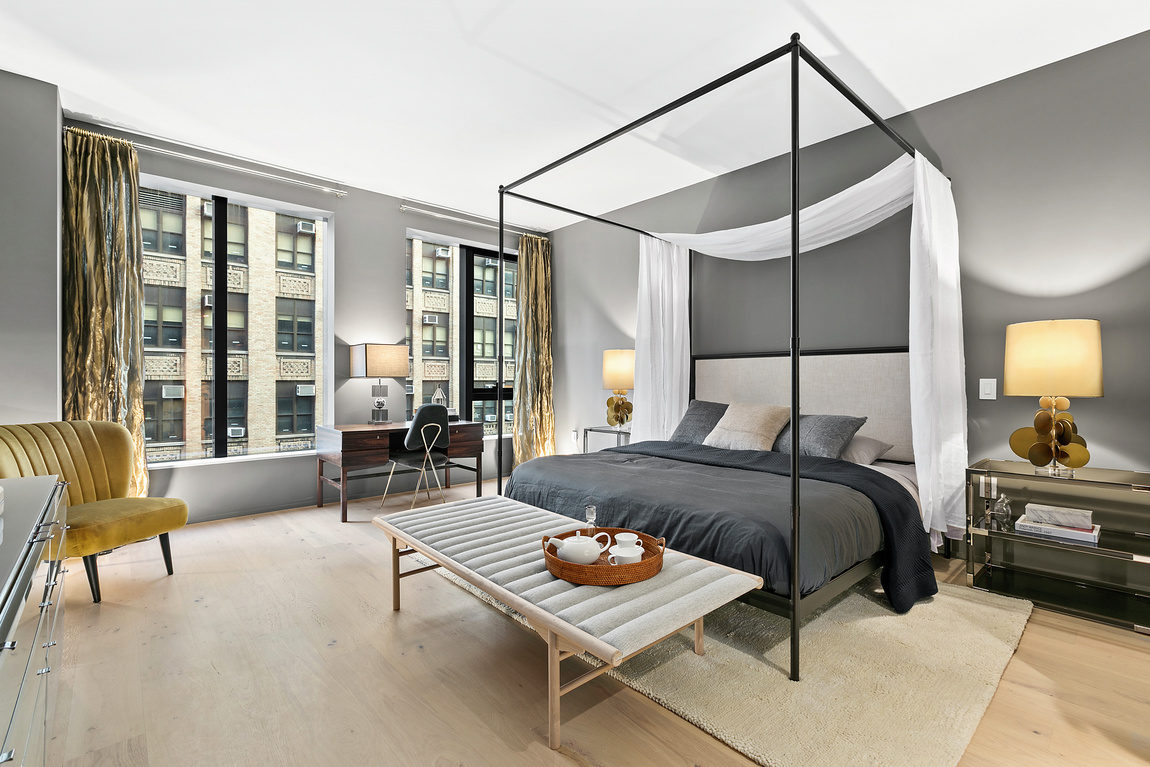 Grey bedroom with four poster bed, modern chairs and light wood flooring. 