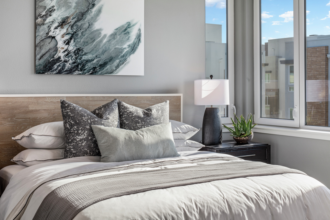 Blue and grey painting above bed with a wooden headboard and white comforter