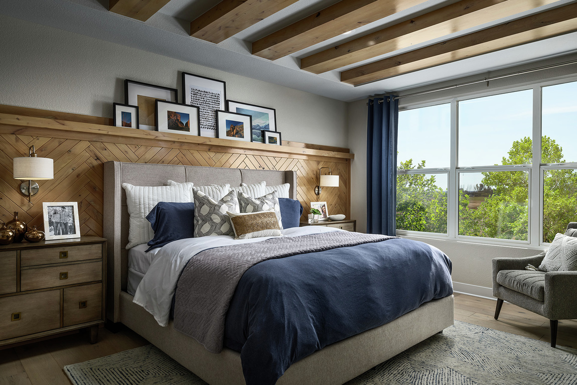 Bedroom with grey paint, bed backboard, wood paneling and ceiling beams. 