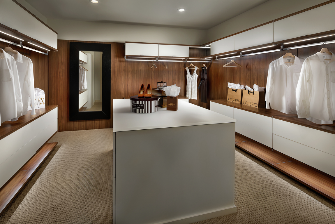 Modern closet with white center island and carpeting with plenty of hanging space. 