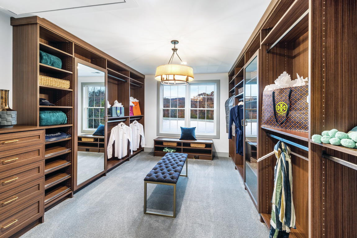 Dark wood closet cabinet finish with chandelier, natural lighting, mirror, and sitting area. 