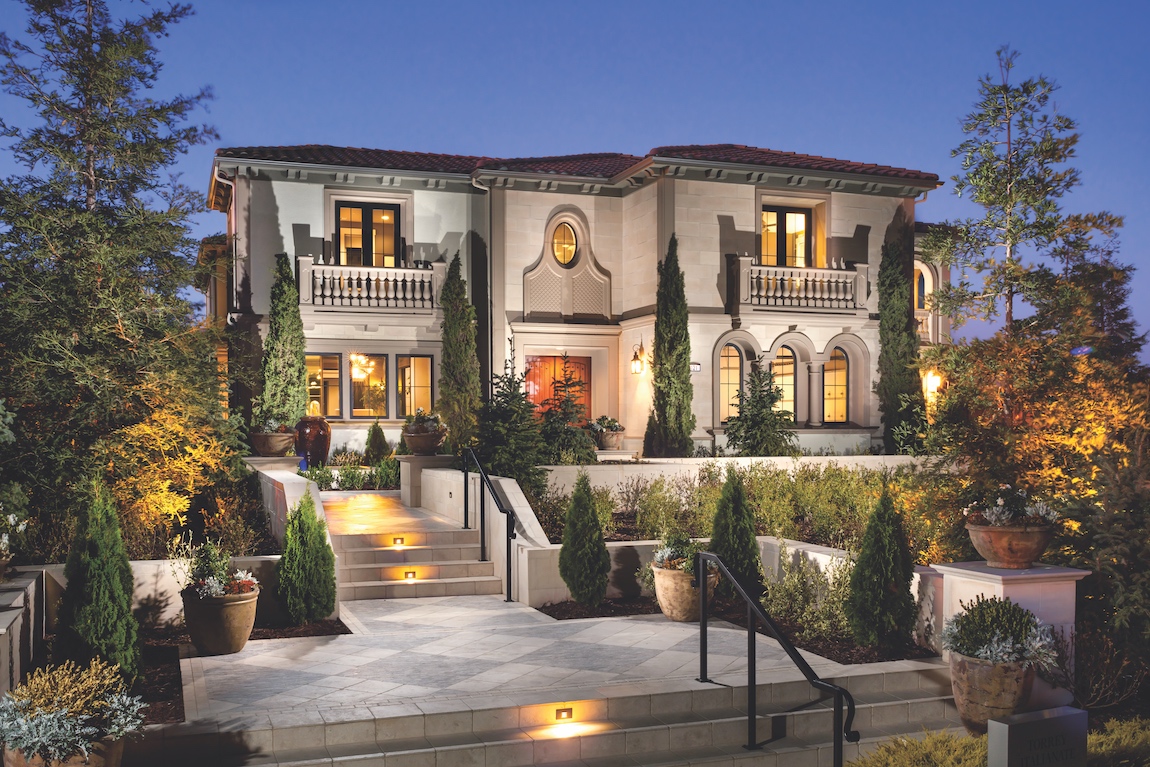 A large luxury home in California with lit up stairs leading to the front door.