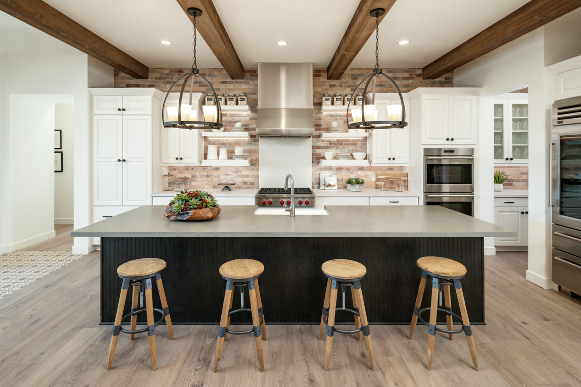 A farmhouse kitchen design with wood ceiling beams and wooden barstools along the large center island.