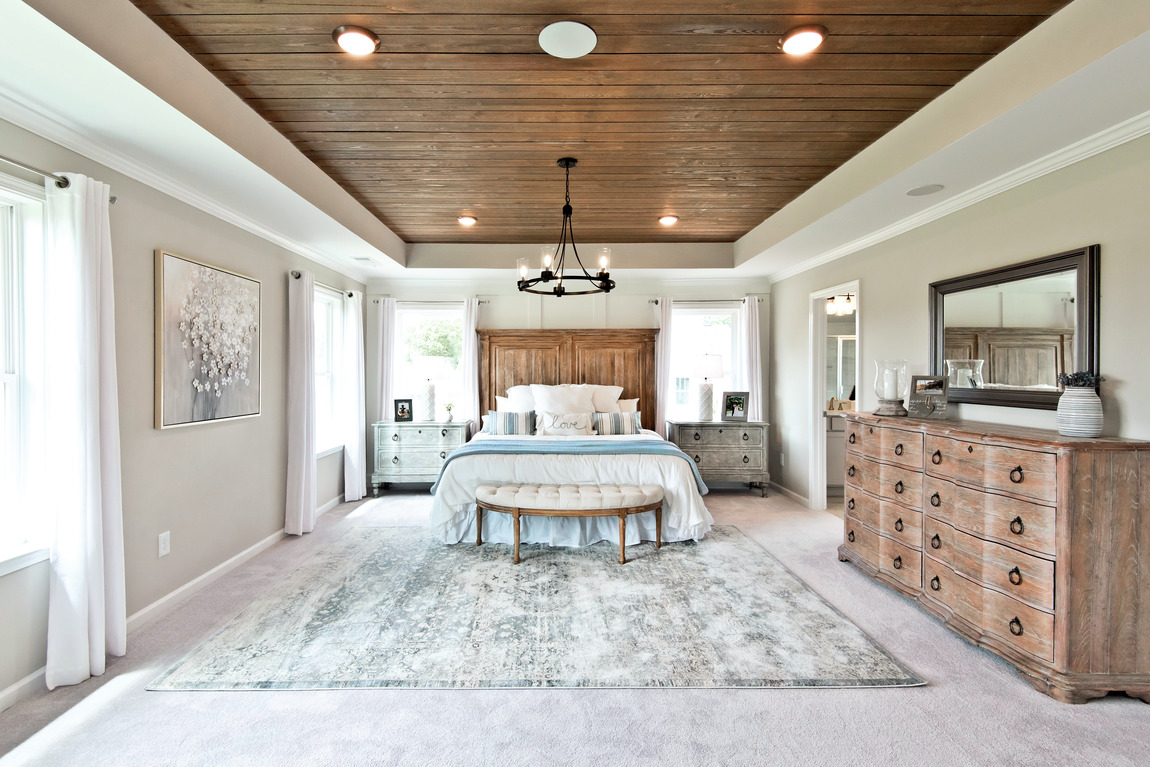 A large primary bedroom with a country style design and a wooden ceiling.
