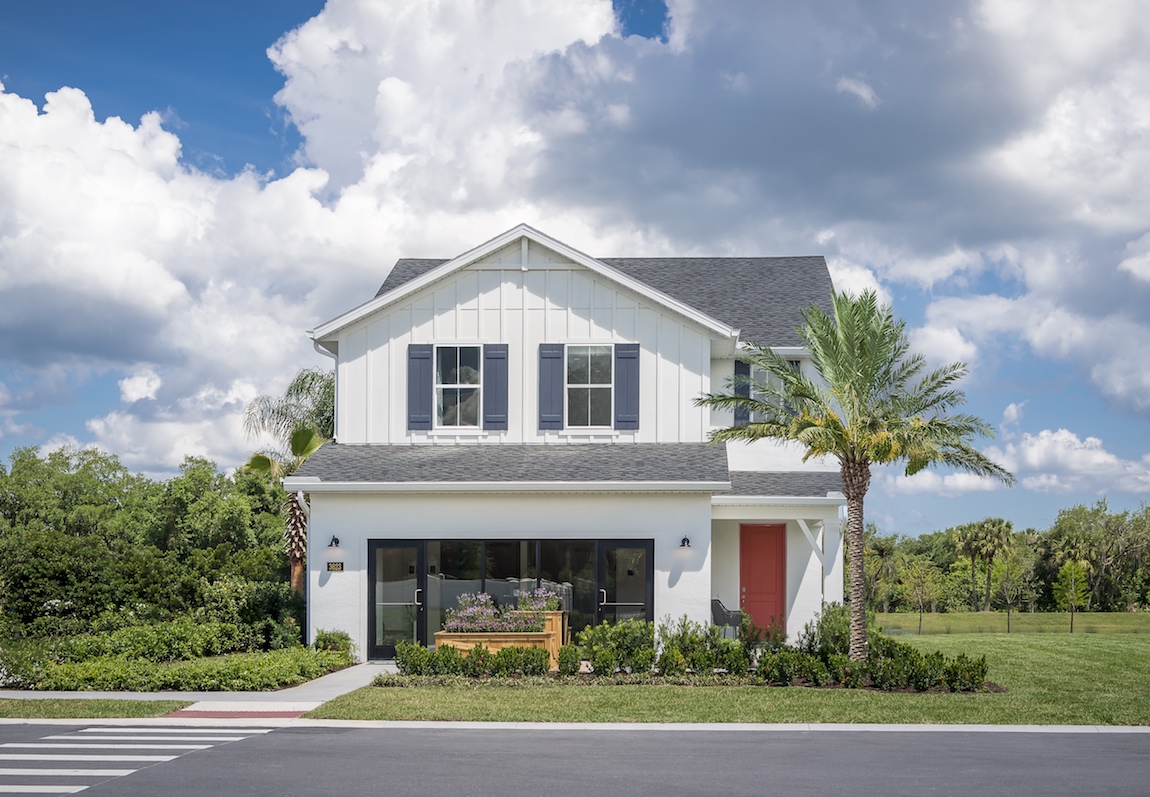 A white Toll Brothers house with a contrasting red door and blue shutters.