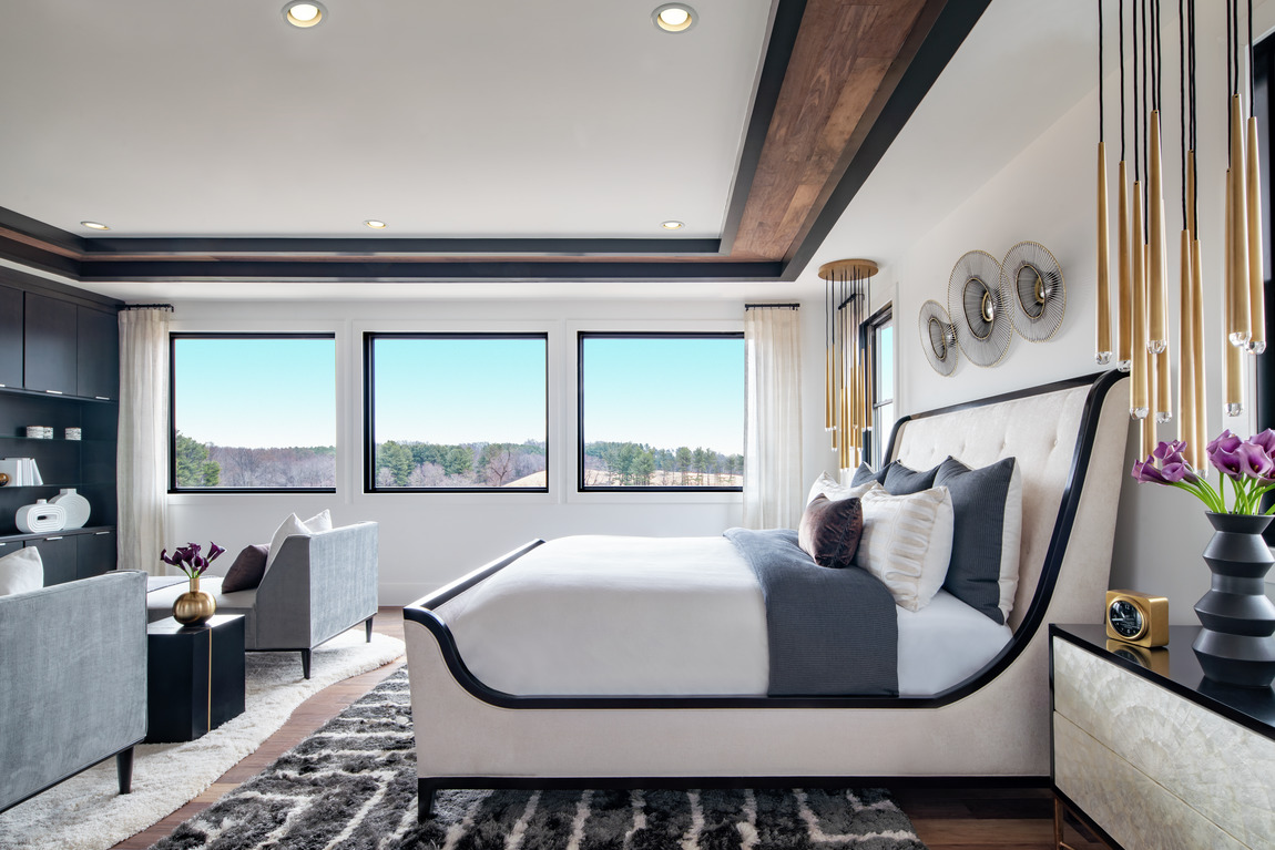 A transitional style bedroom with a patterned rug and a seating area in a luxury home.