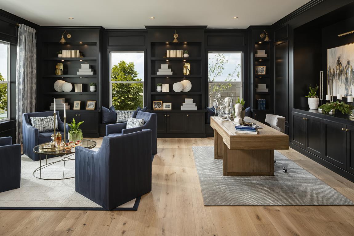 Home office with black floor to ceiling shelving, sitting area with blue arm chairs and light colored desk