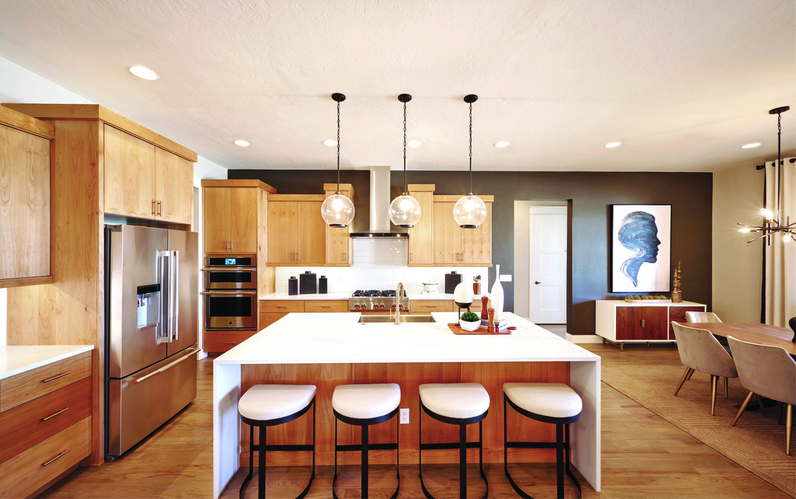 Light brown modern kitchen with white countertop, spacious island, pendant lighting, and metal barstools with white cushion