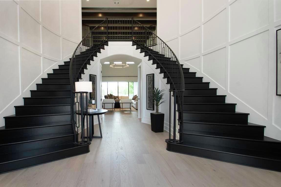 Black dual staircase paired with coffered wall accents in spacious foyer design