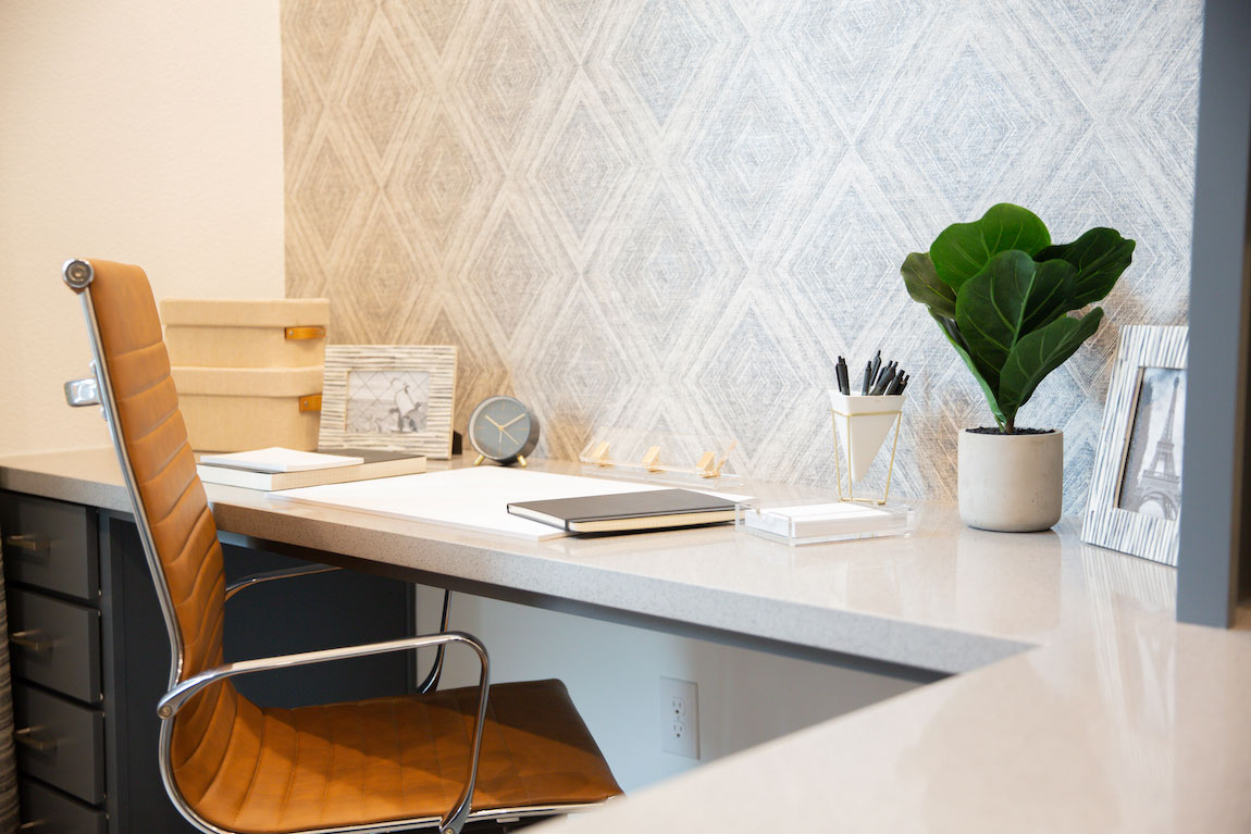 Desk with modern leather chair, clock, and fiddle plant. 