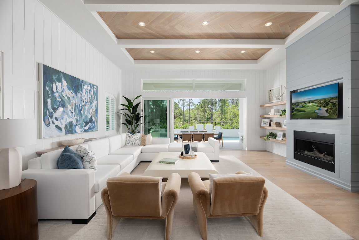 Living room with television, sofa, brown arm chairs, engineered hardwood flooring and view to outdoor living patio. 