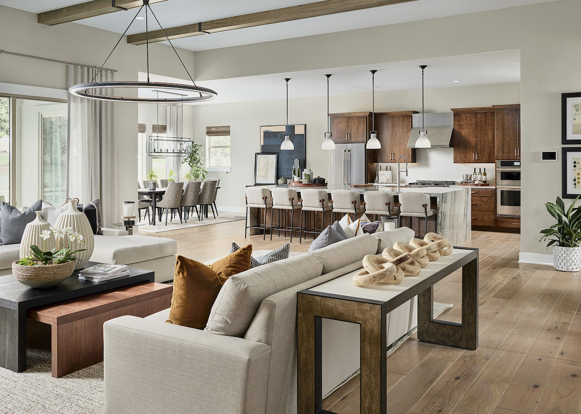 Living room with view of two-toned wooden cabinets, neutral colored sofa and wood beam ceilings with engineered hardwood flooring. 