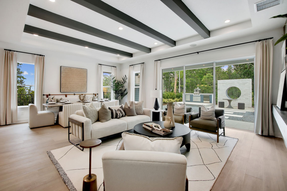 Living room with black beam ceiling and neutral wood floors with view to the backyard. 