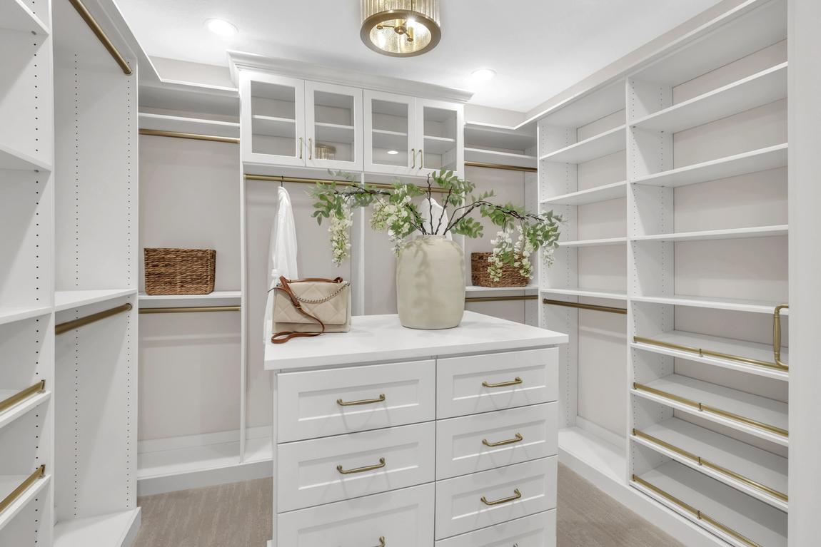Luxury design closet with white cabinetry, gold accented medal and chandelier. 
